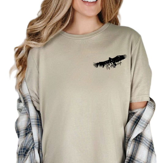 A person wearing a beige softstyle tee with a pocket design featuring an eagle and mountains.