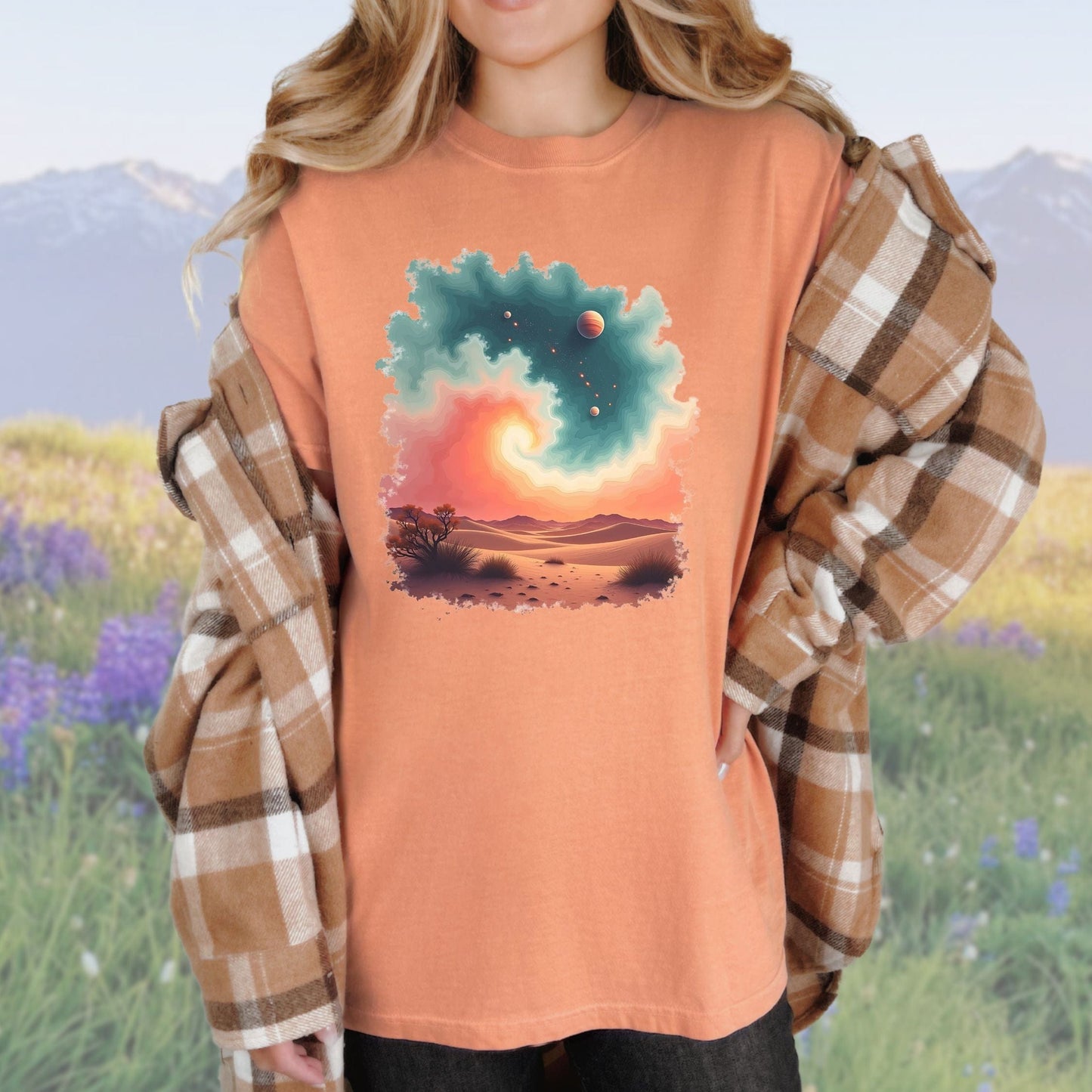 A woman wearing a vintage-style terracotta colored tee with a desert swirl pattern, paired with a plaid shirt.