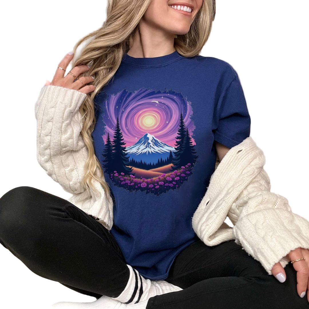 A person sitting and modeling a blue t-shirt with a vintage-style mountain and starry sky design.