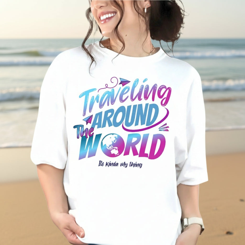 A person standing by the beach wearing a black t-shirt with the text 'Traveling Around The World' in a colorful, vintage-style font.