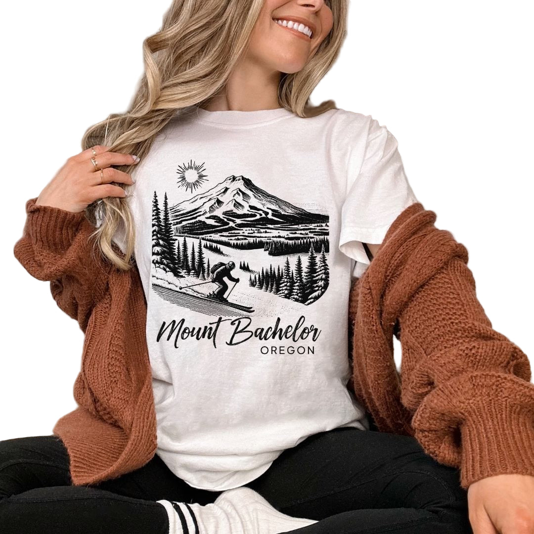 A woman smiling and wearing a white t-shirt with 'Mount Bachelor Oregon' text and a mountain graphic design.