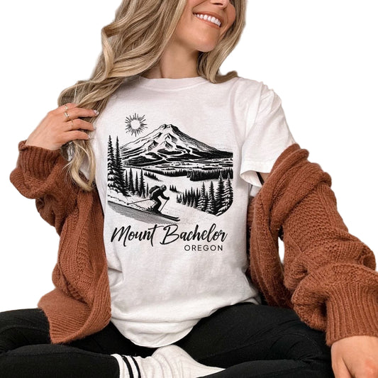 A woman smiling and wearing a white t-shirt with 'Mount Bachelor Oregon' text and a mountain graphic design.