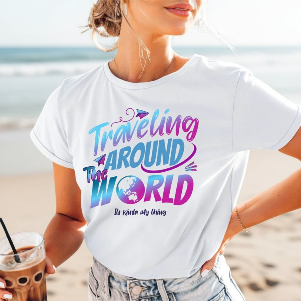 A woman wearing a white T-shirt with the text 'Traveling Around the World' printed on it, standing by the beach.