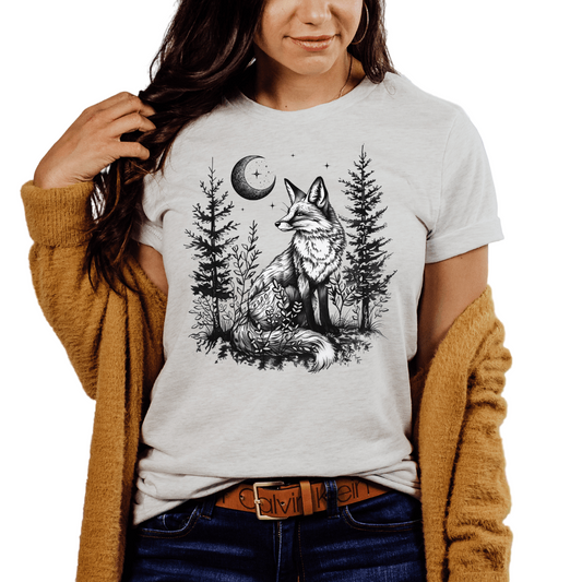 A woman wearing an ash colored t-shirt with a black printed design of a fox, trees, and moon.