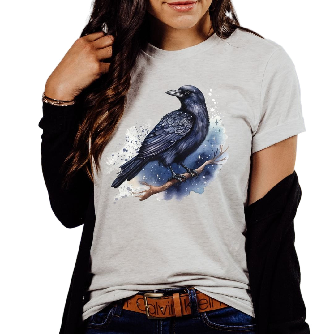 A person wearing an ash colored t-shirt with a nature-inspired design featuring a raven.