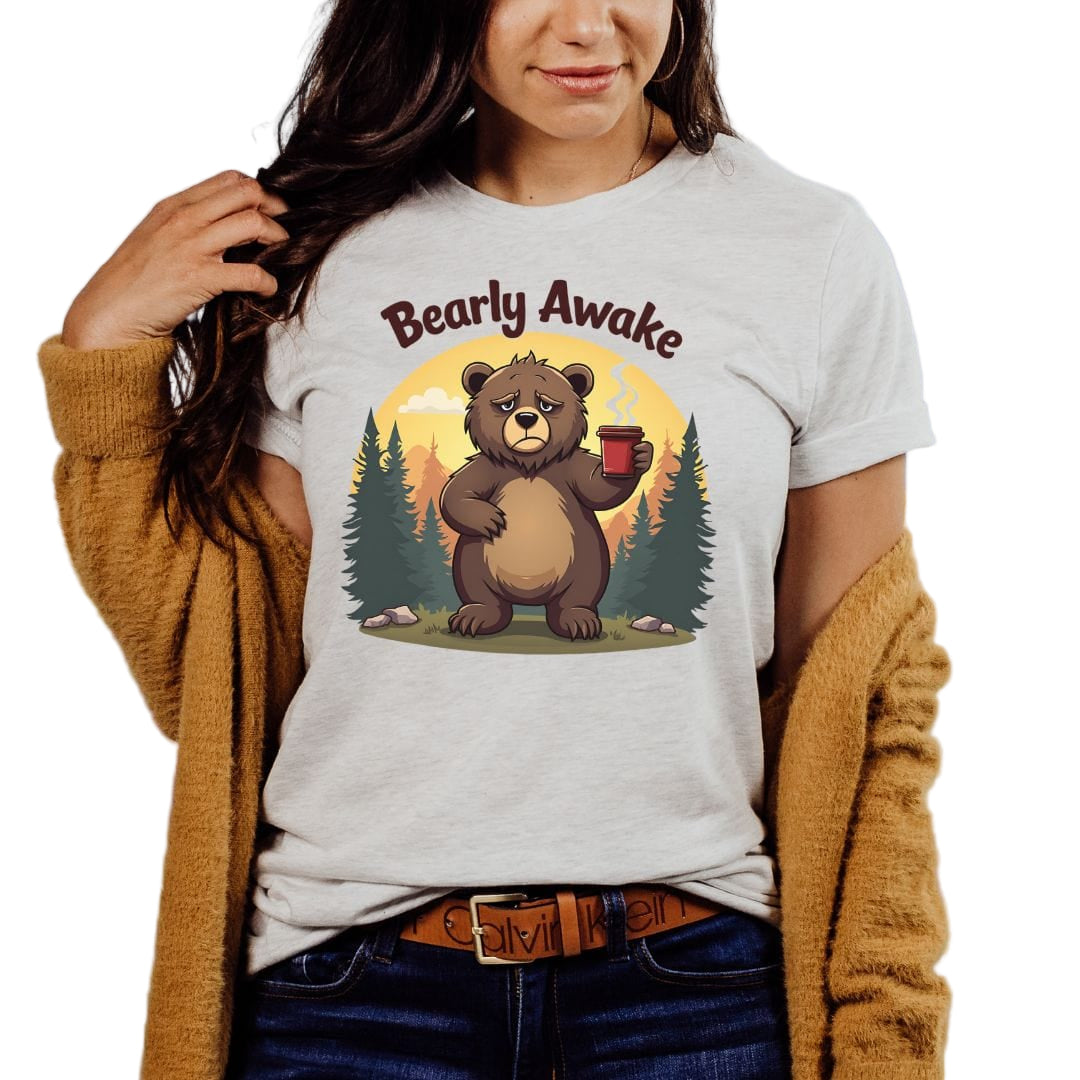 A woman wearing a gray 'Bearly Awake' sleepy bear t-shirt with a graphic of a bear holding a mug.