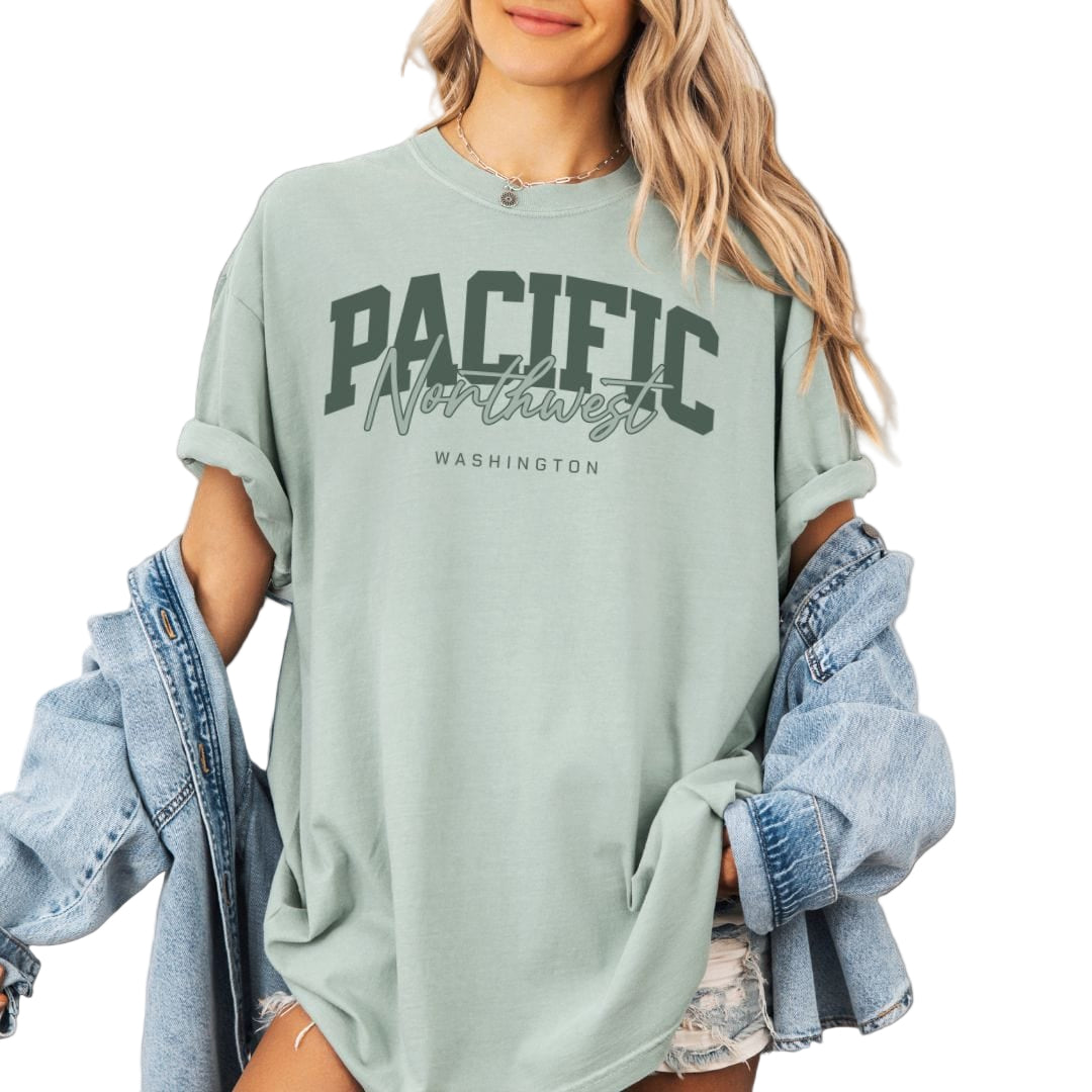 Person wearing a light green sweatshirt with 'Pacific Northwest Washington' text, holding a denim jacket.