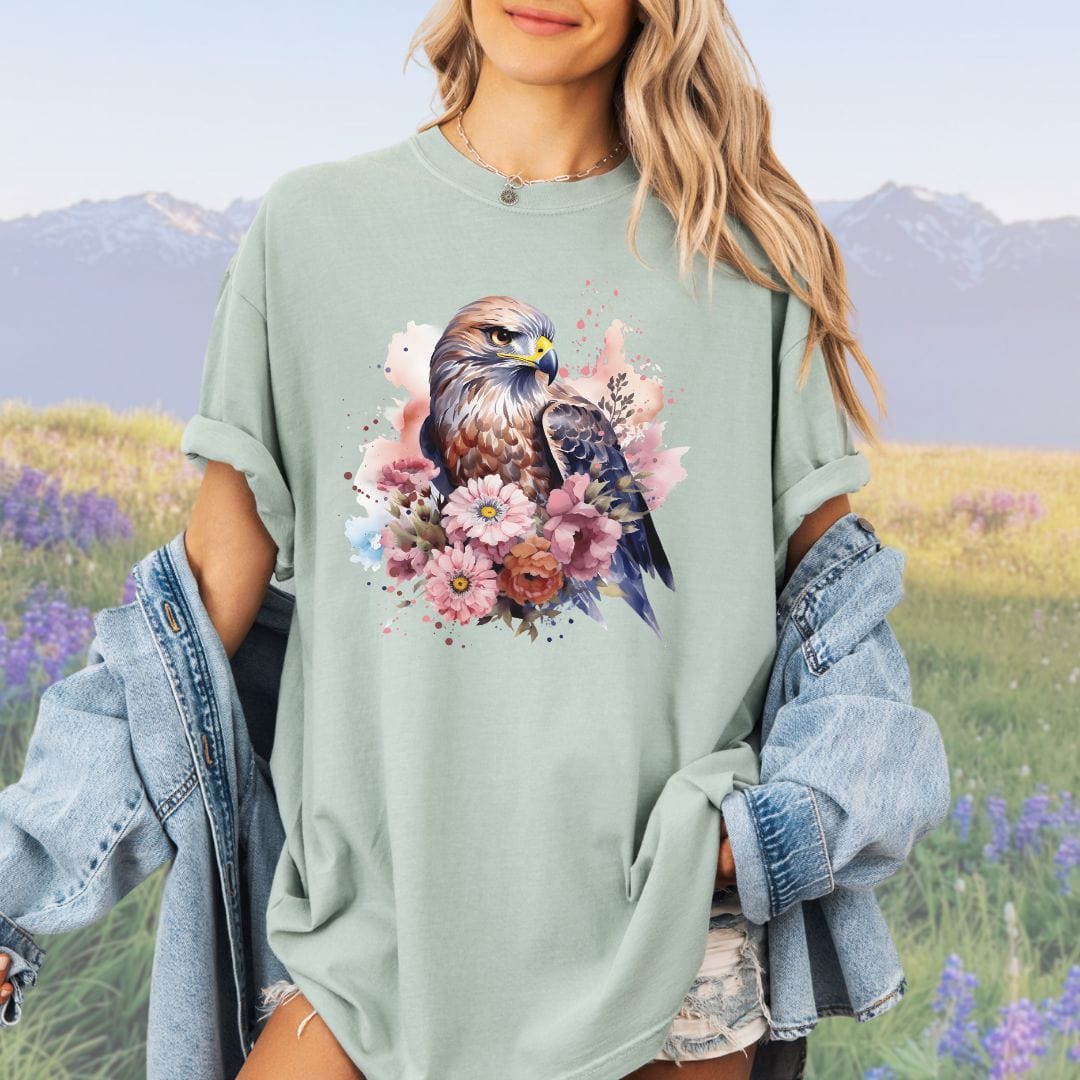 A person wearing a vintage-style light green shirt with a graphic print of a bird of prey surrounded by flowers.