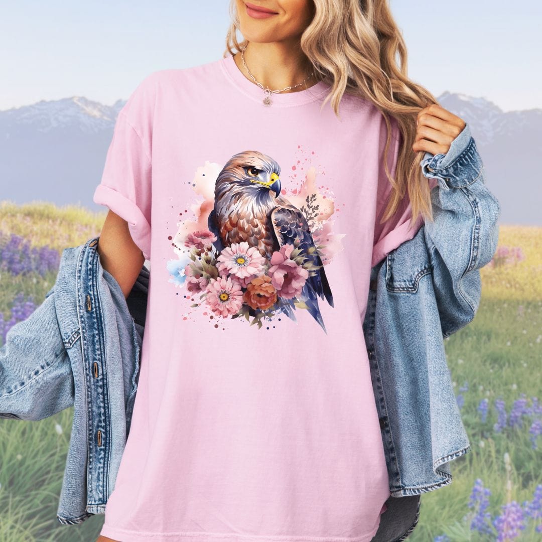 A person wearing a vintage-style pink t-shirt with a graphic print of a bird of prey surrounded by flowers.