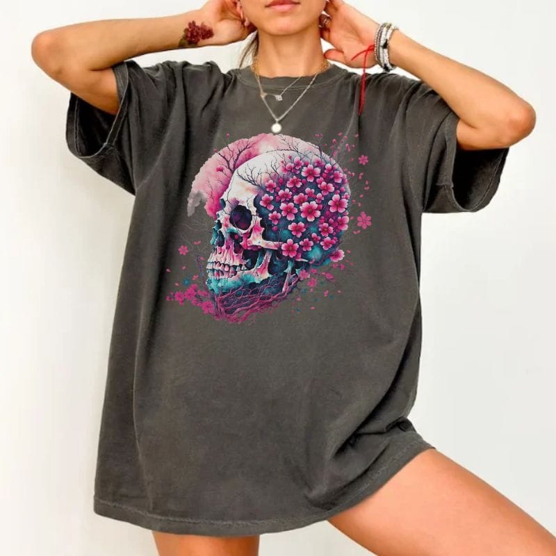 A woman wearing an oversized dark gray t-shirt with a colorful skull and pink flower graphic on the front, posed against a plain white background.