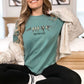 Woman wearing a light green, Find Your Flock Comfort Colors T-shirt with perched bird graphic and inspirational friendship phrase