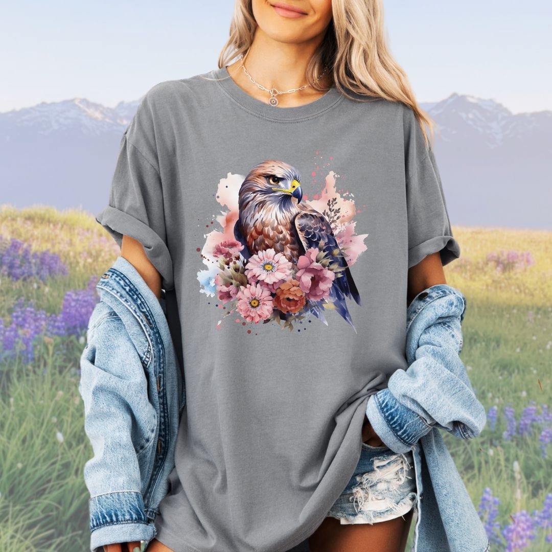 A person wearing a vintage-style gray t-shirt with a graphic print of a bird of prey surrounded by flowers.