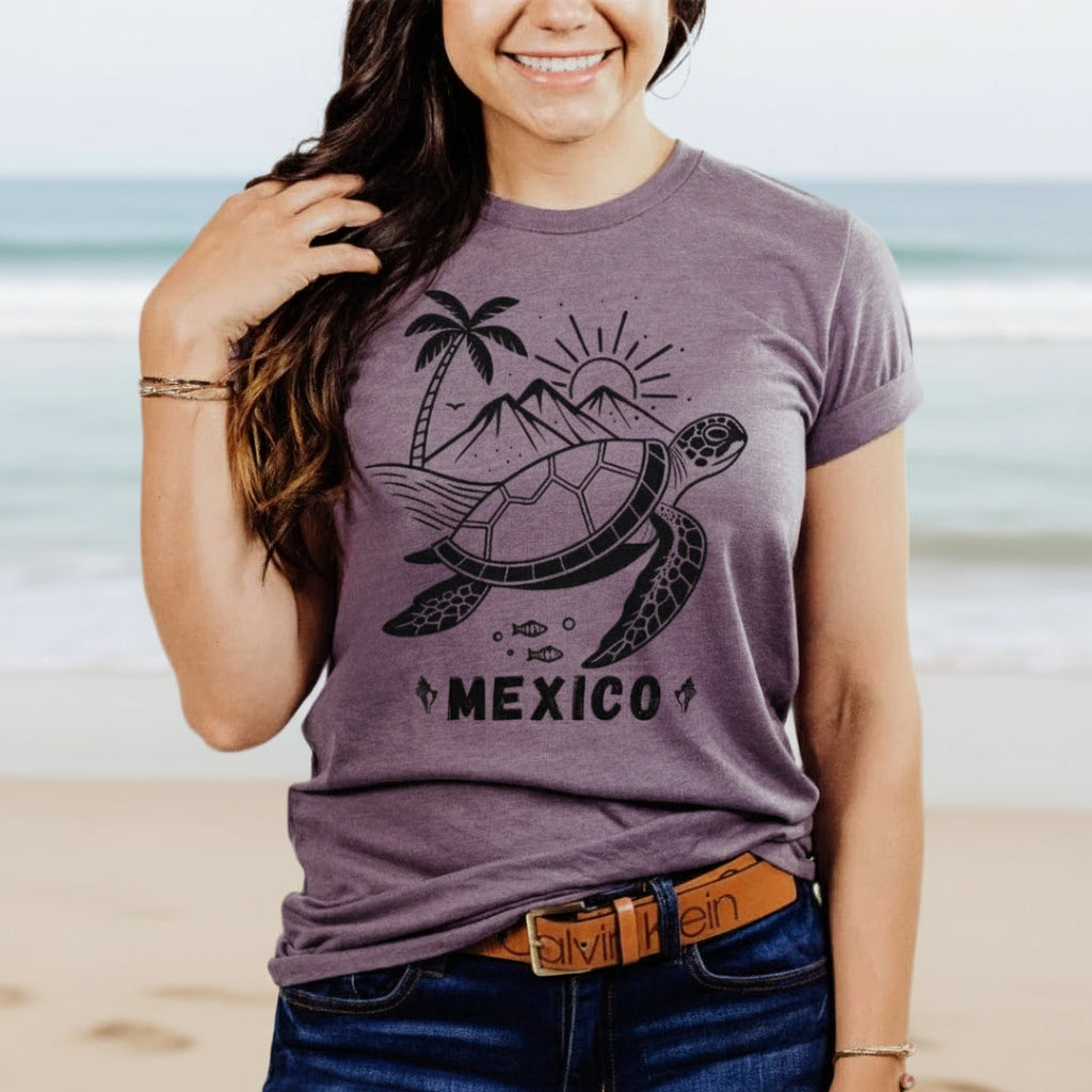 A woman wearing a soft purple crew neck t-shirt with a graphic of a turtle, palm trees, and the word 'MEXICO' on it.