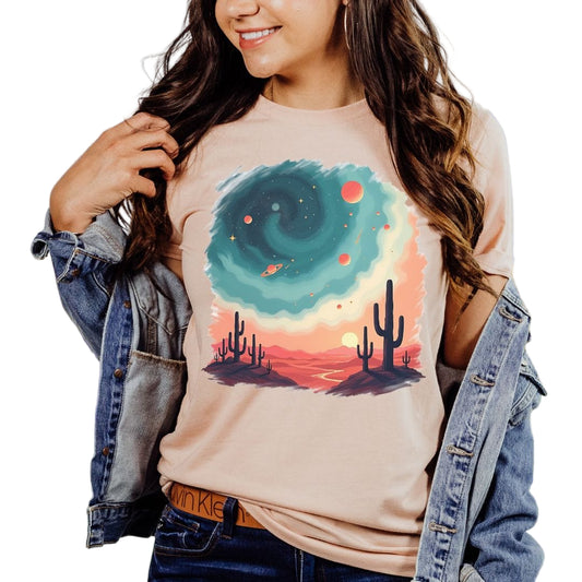 A person wearing a peach t-shirt with a nature-inspired design, including silhouettes of cacti and a cosmic pattern in the background.