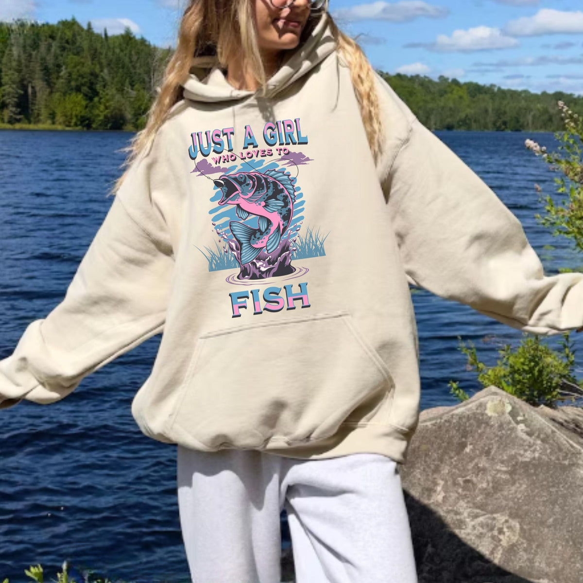 Person wearing a hoodie with a fish graphic and text by a lake