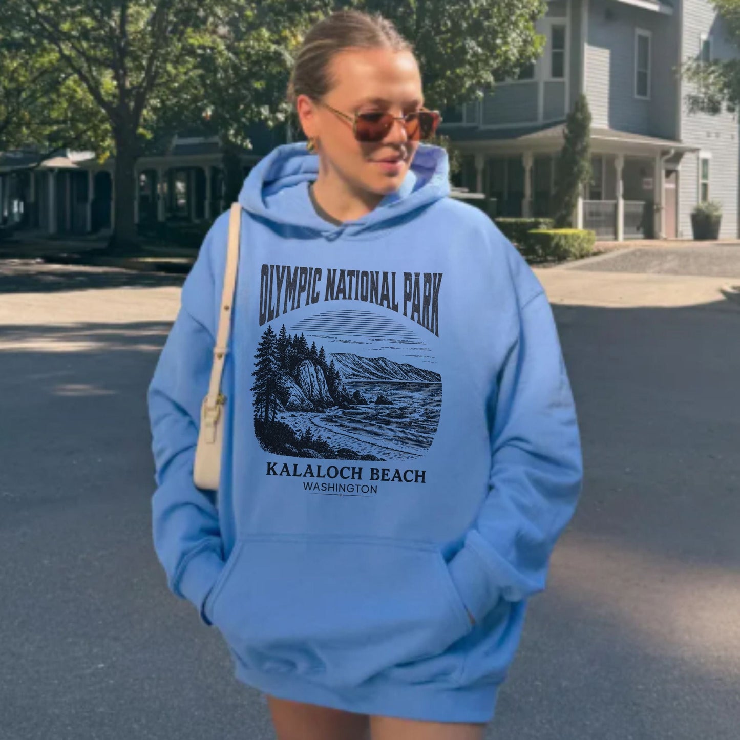 Person wearing a blue hoodie with Olympic National Park design outdoors.