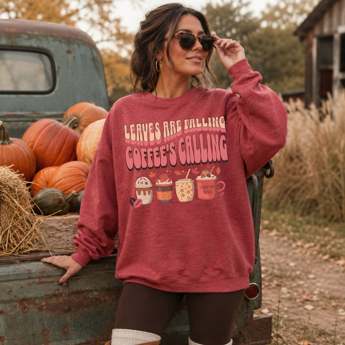 Woman wearing a washed red fall sweatshirt with coffee cups, pumpkins, autumn leaves, and Leaves Are Falling Coffee’s Calling design