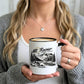 A person holding a white ceramic mug with a black rim, handle, and printed black mountain landscape design labeled 'Mt. Rainier National Park - Washington.