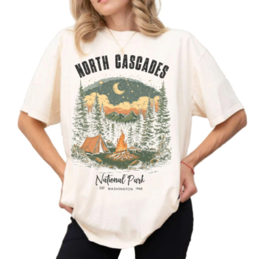 Woman wearing an ivory Comfort Colors t-shirt featuring a colorful retro illustration of a campfire and tent at North Cascades National Park Washington.