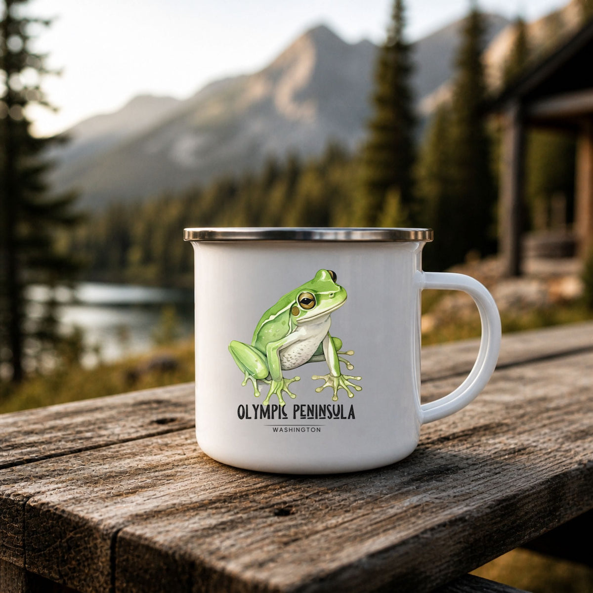 White enamel camp mug with a green frog illustration and Olympic Peninsula, Washington lettering, displayed outdoors on a wooden bench.