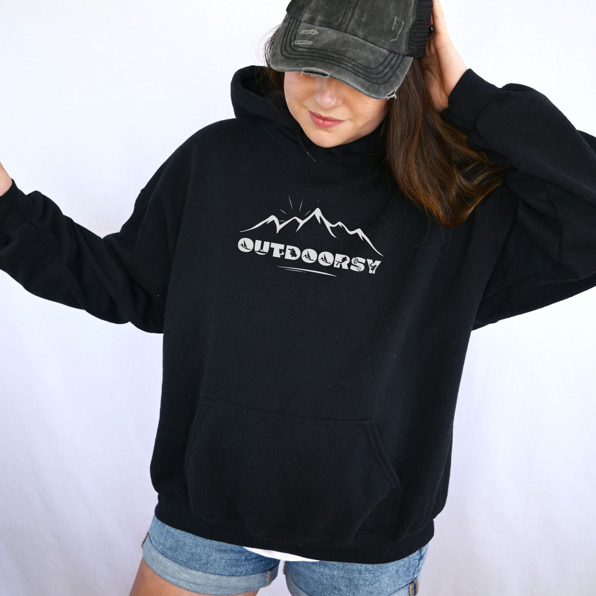 Person wearing a black hoodie with 'OUTDOORSY' text and mountain graphic on a white background