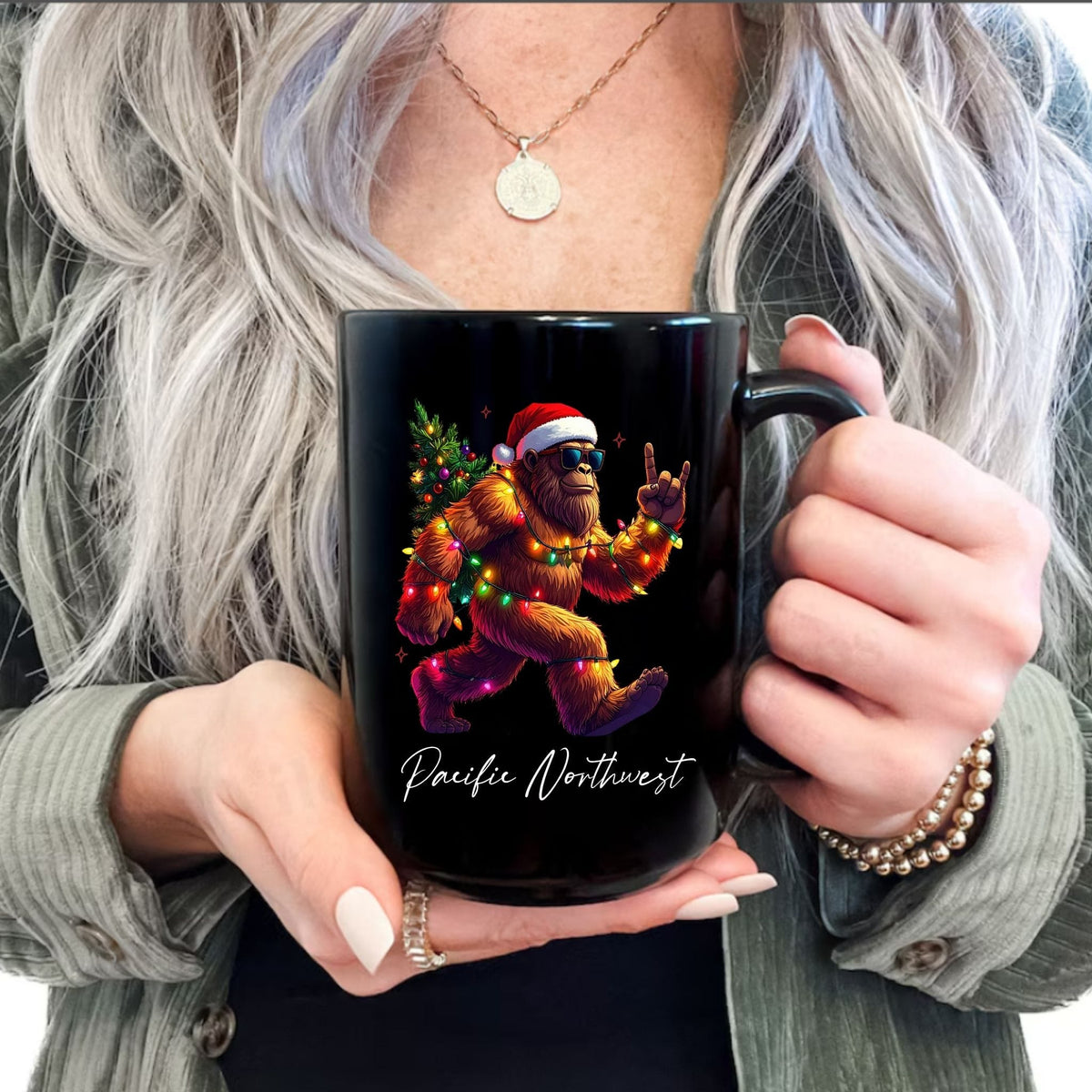 A person holding a black ceramic mug with a colorful graphic of a Santa-clad dancing bear and the text 'Pacific Northwest' on the front.
