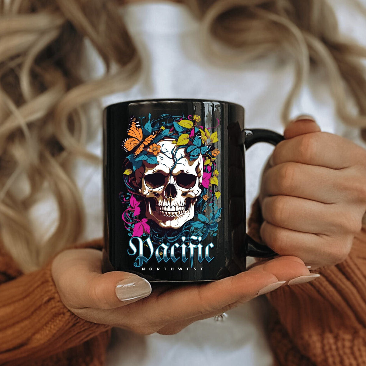 Person holding a black mug with a colorful skull design and text.
