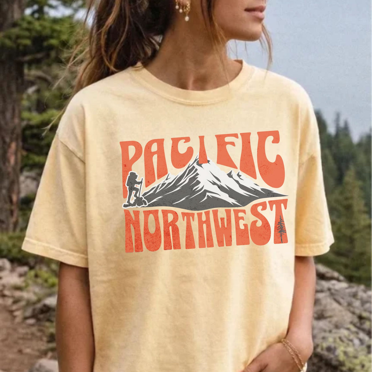 A woman wearing a Pacific Northwest mountain hiking T-shirt with vintage orange graphic on a yellow garment-dyed tee.