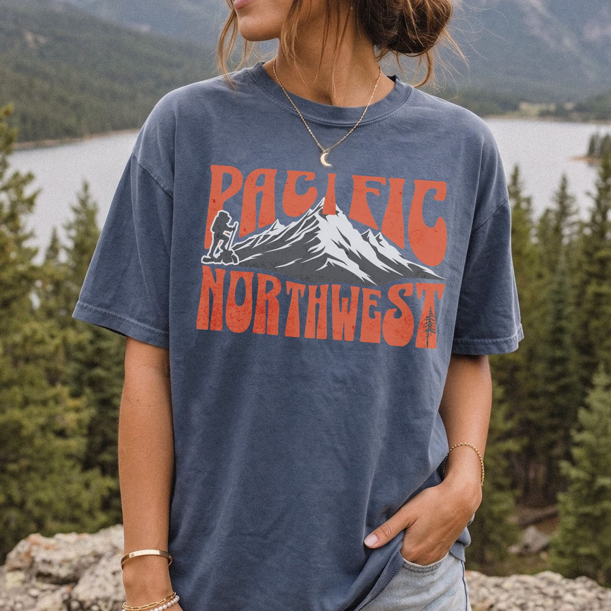 A woman wearing a Pacific Northwest mountain hiking T-shirt with vintage orange graphic on a blue garment-dyed tee.