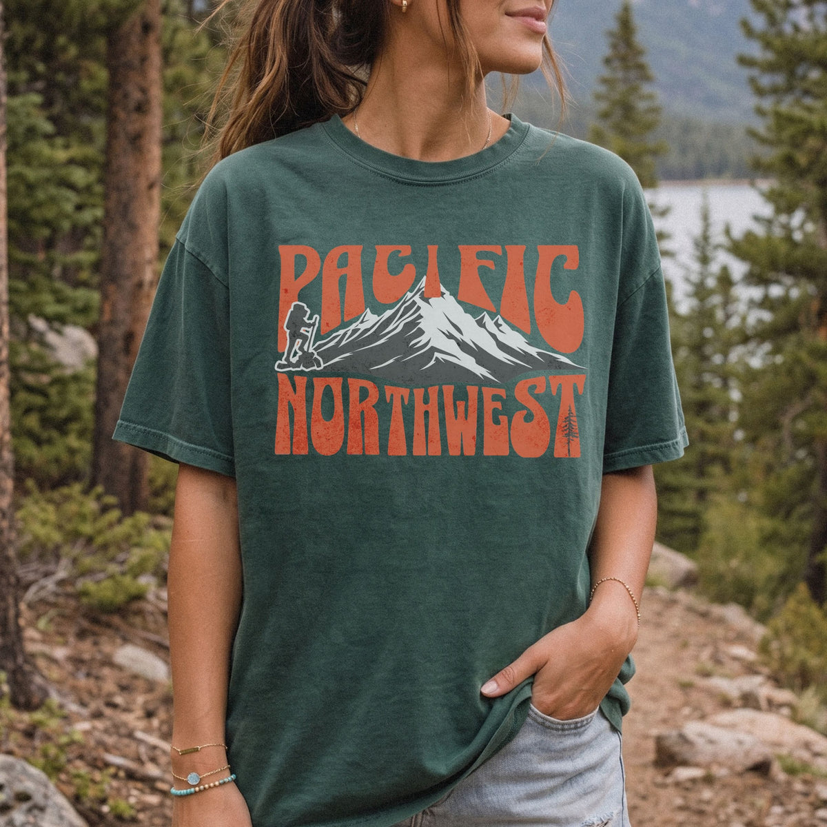 A woman wearing a Pacific Northwest mountain hiking T-shirt with vintage orange graphic on a green garment-dyed tee.
