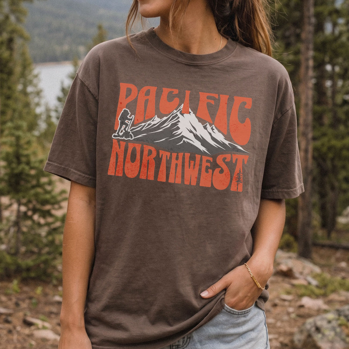 A woman wearing a Pacific Northwest mountain hiking T-shirt with vintage orange graphic on a brown garment-dyed tee.