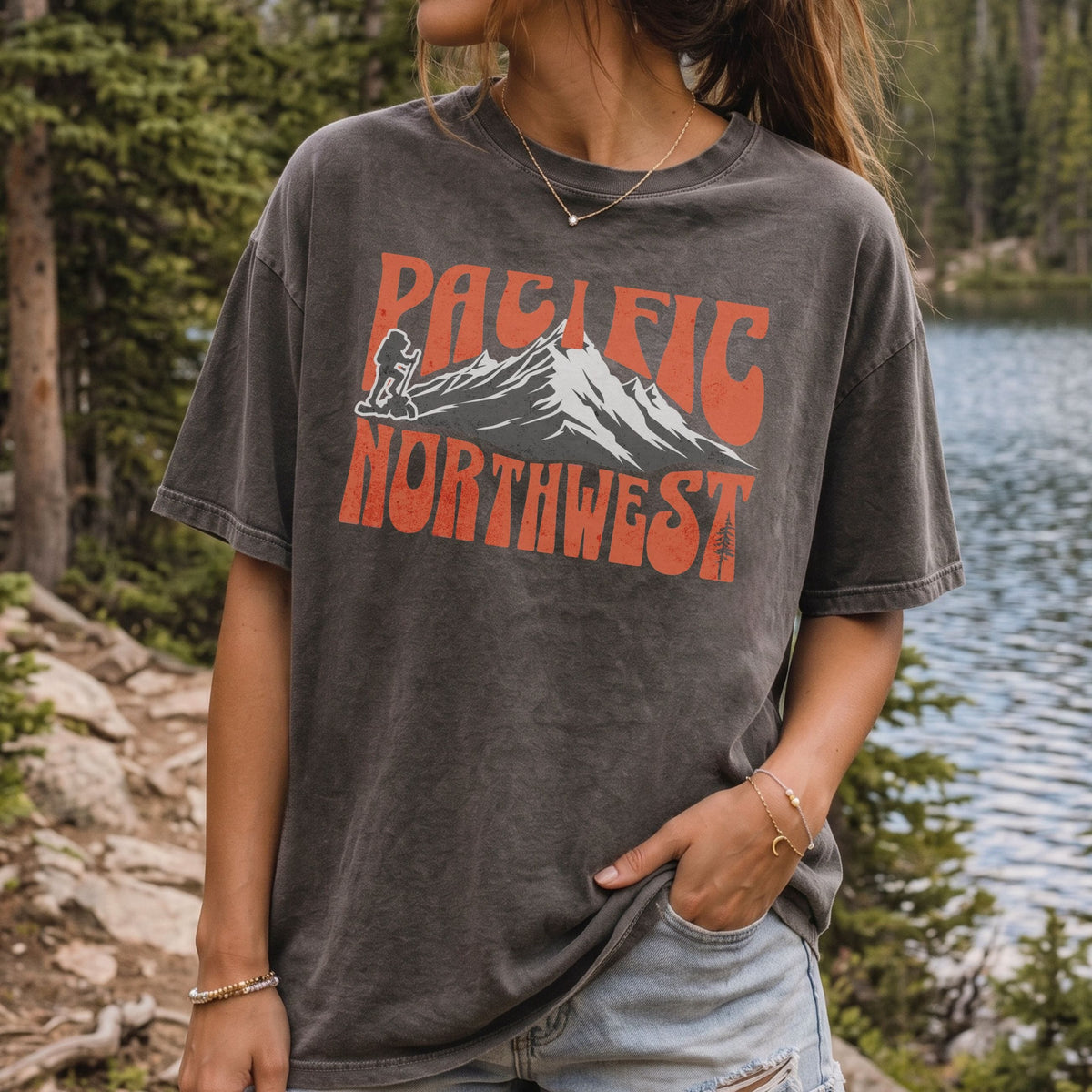 A woman wearing a Pacific Northwest mountain hiking T-shirt with vintage orange graphic on a dark gray garment-dyed tee.