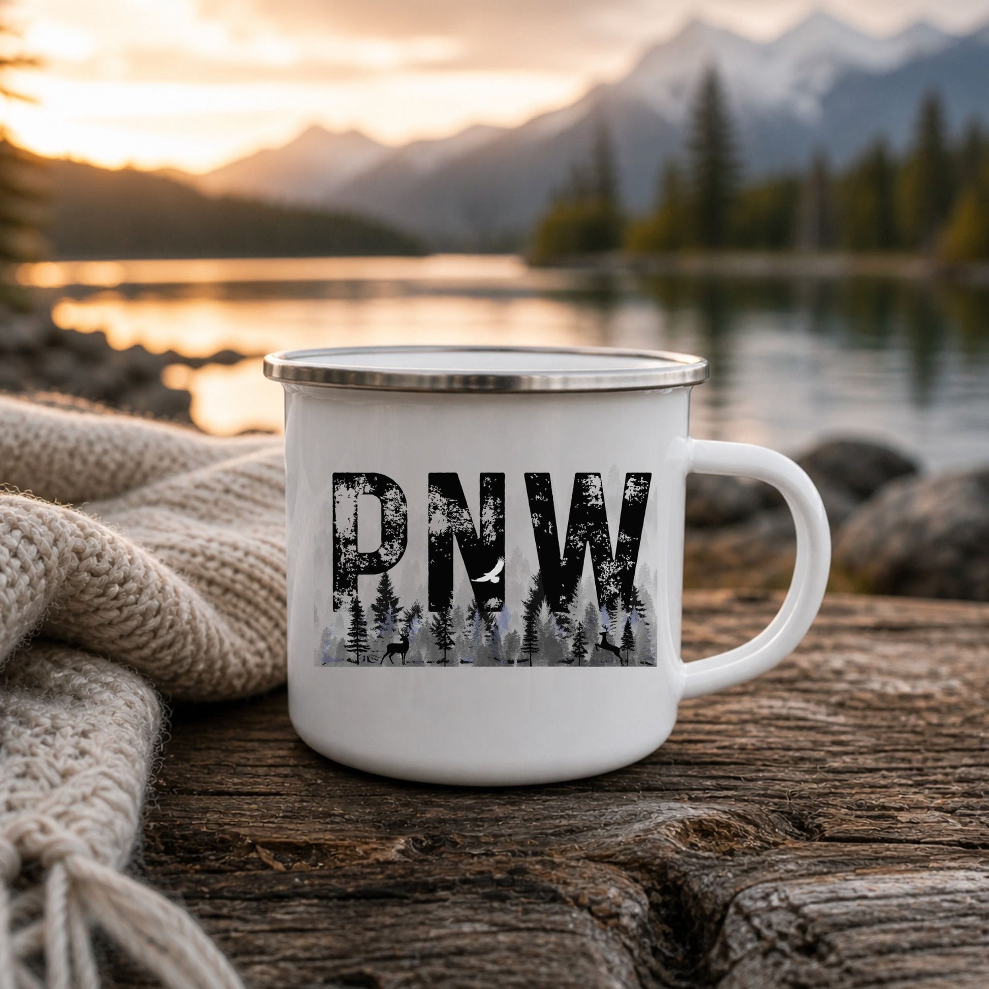 White enamel PNW forest camp mug on a wooden table beside a mountain lake