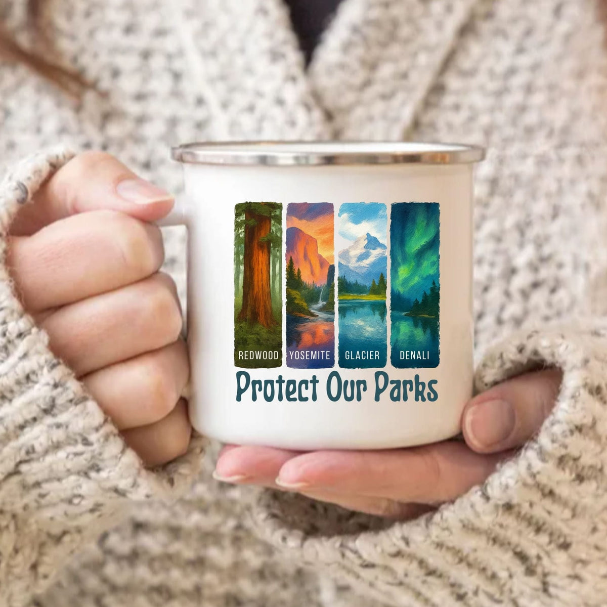 A person in a beige knit sweater holds a white enamel-style mug with a silver rim. The mug features four colorful national park illustrations labeled Redwood, Yosemite, Glacier, and Denali, with the text 'Protect Our Parks' below.