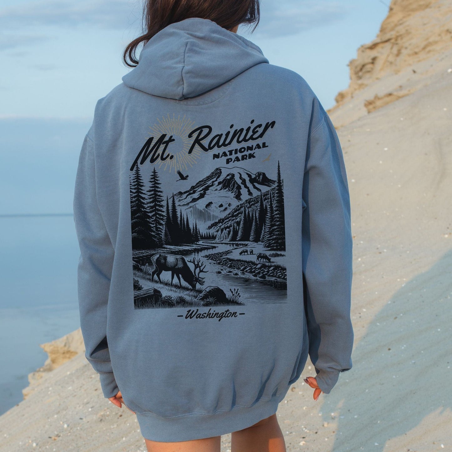 Person wearing a hoodie with Mt. Rainier National Park design outdoors.