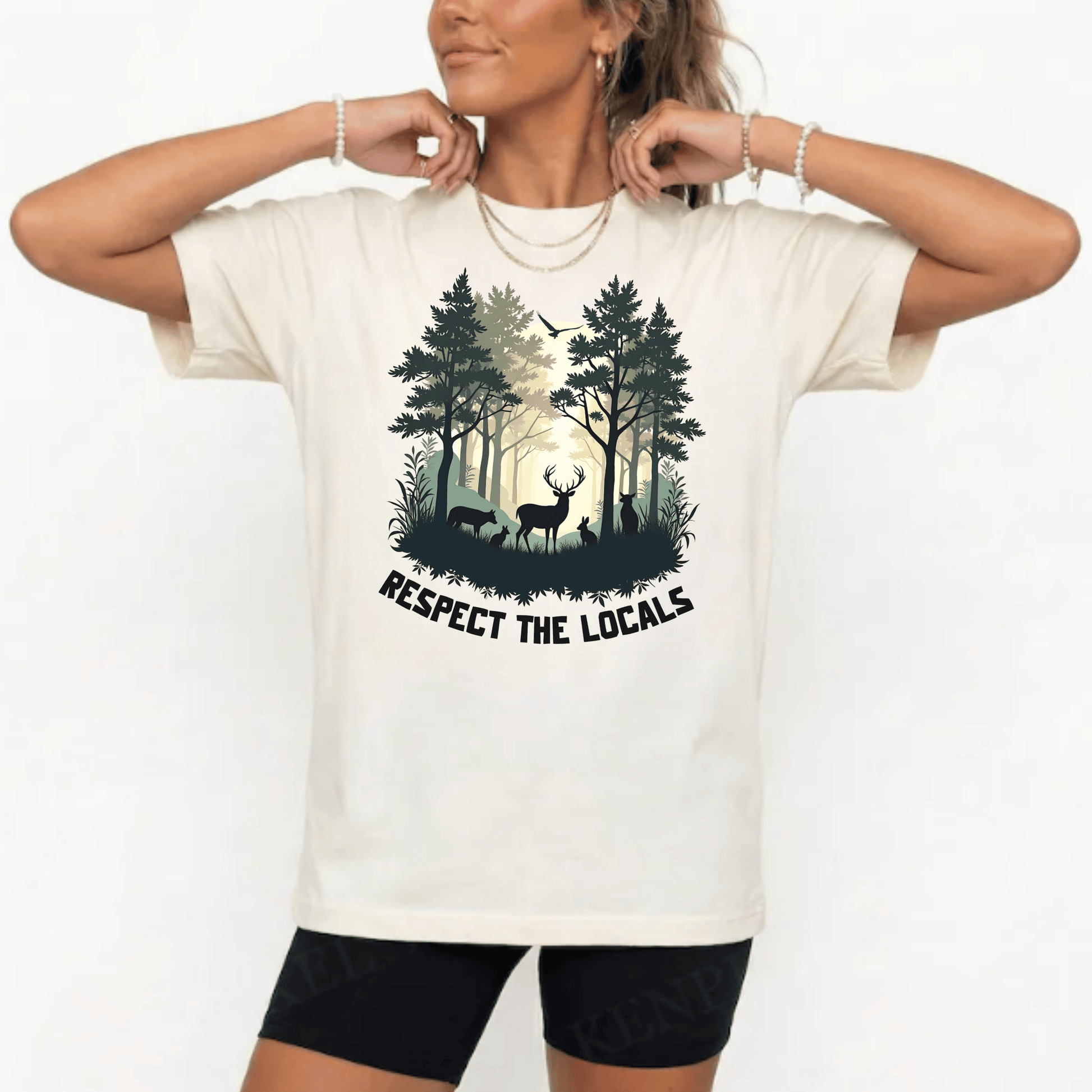 A woman wearing a cream-colored graphic t-shirt with a forest design and the text 'RESPECT THE LOCALS'. The background is a clean white studio setting.