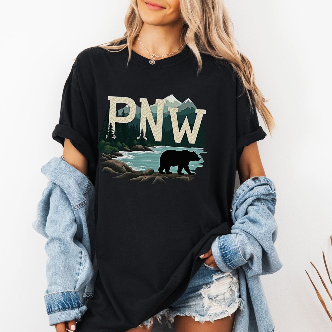 Woman wearing a black t-shirt with PNW graphic featuring a bear and mountains on a white background