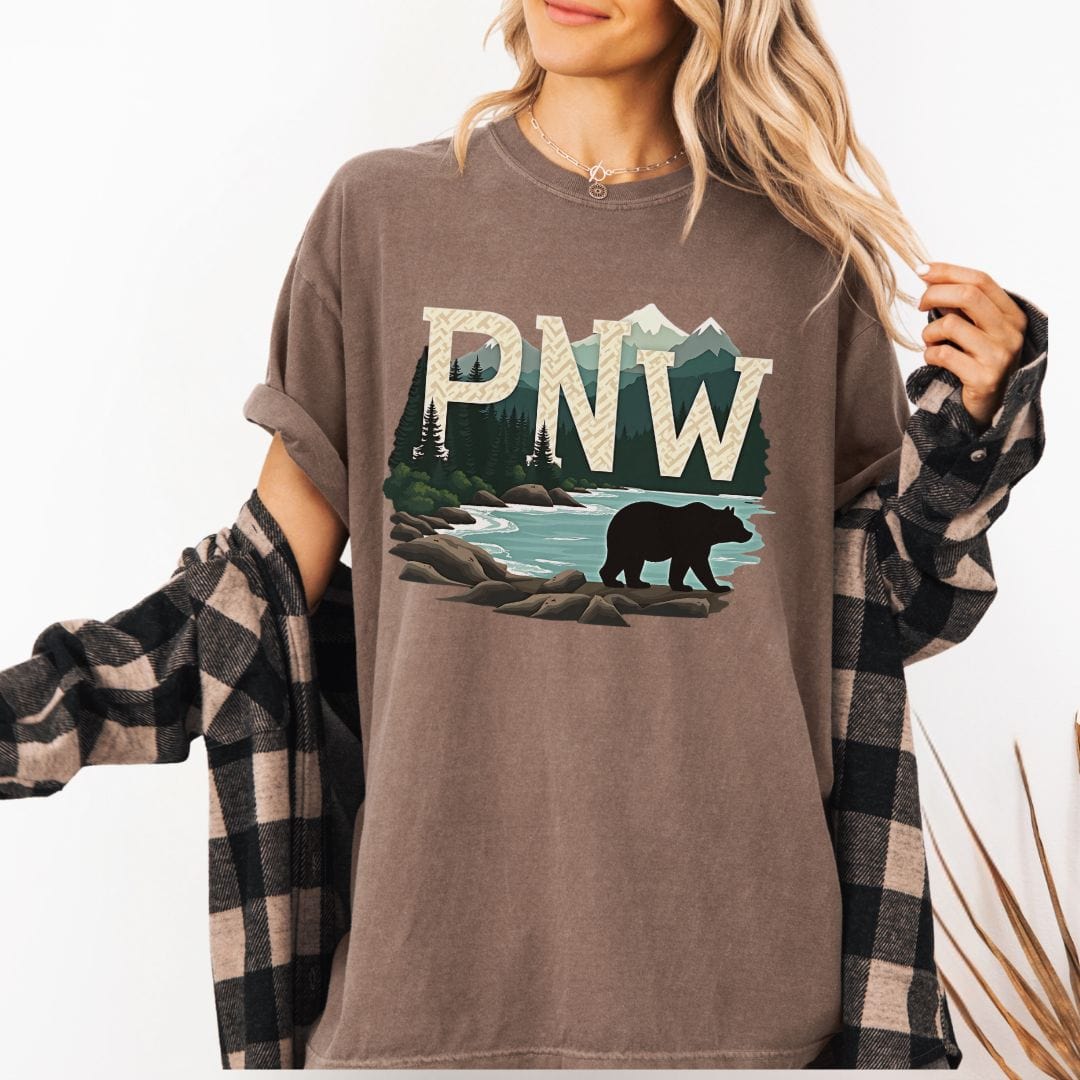 Woman wearing a brown t-shirt with PNW graphic featuring a bear and mountains on a white background