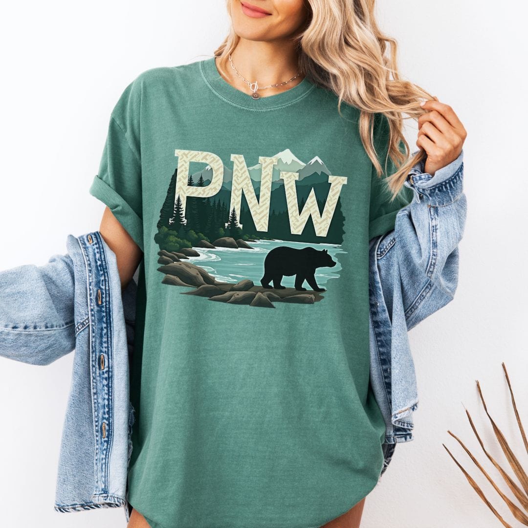 Woman wearing a light green t-shirt with PNW graphic featuring a bear and mountains on a white background