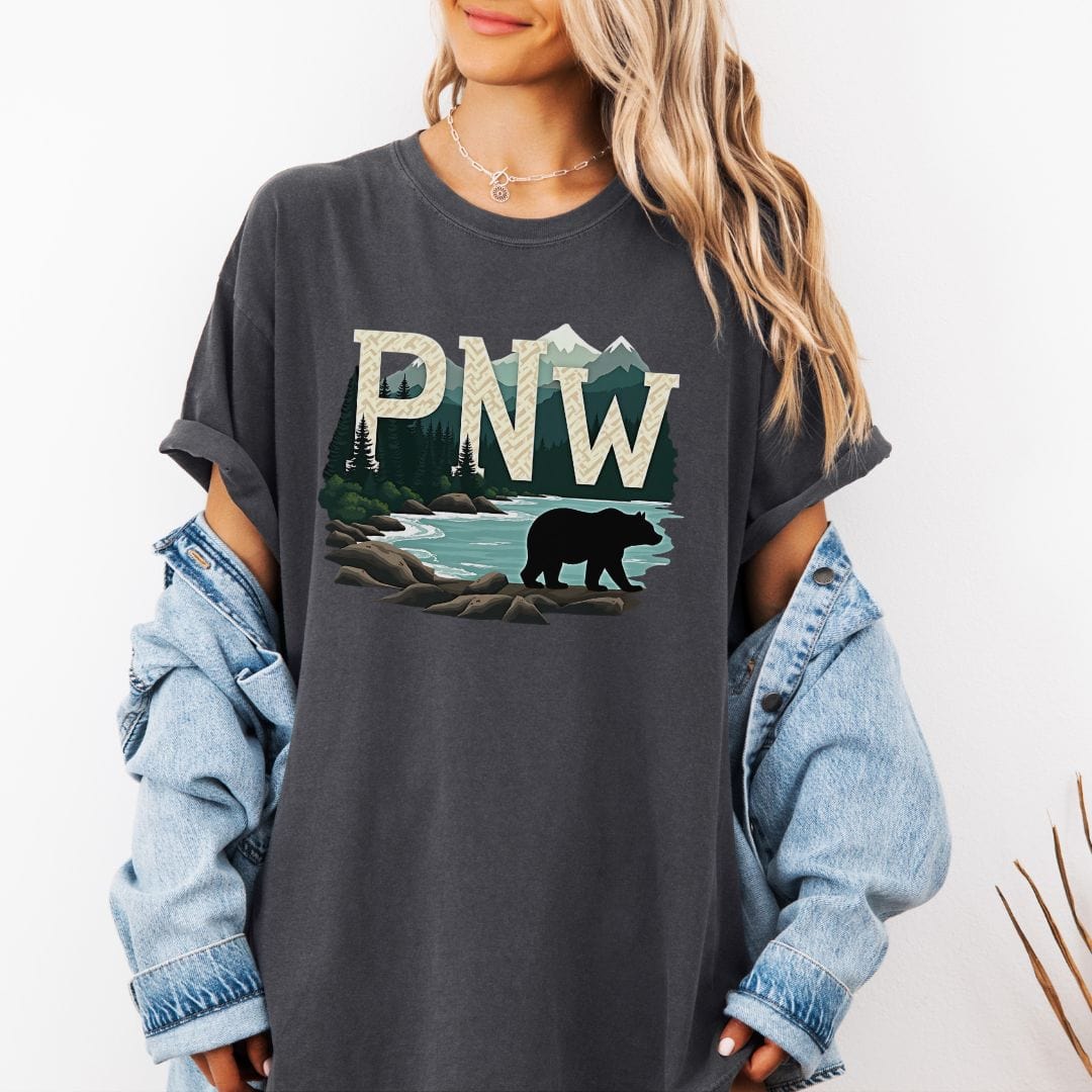 Woman wearing a charcoal t-shirt with PNW graphic featuring a bear and mountains on a white background