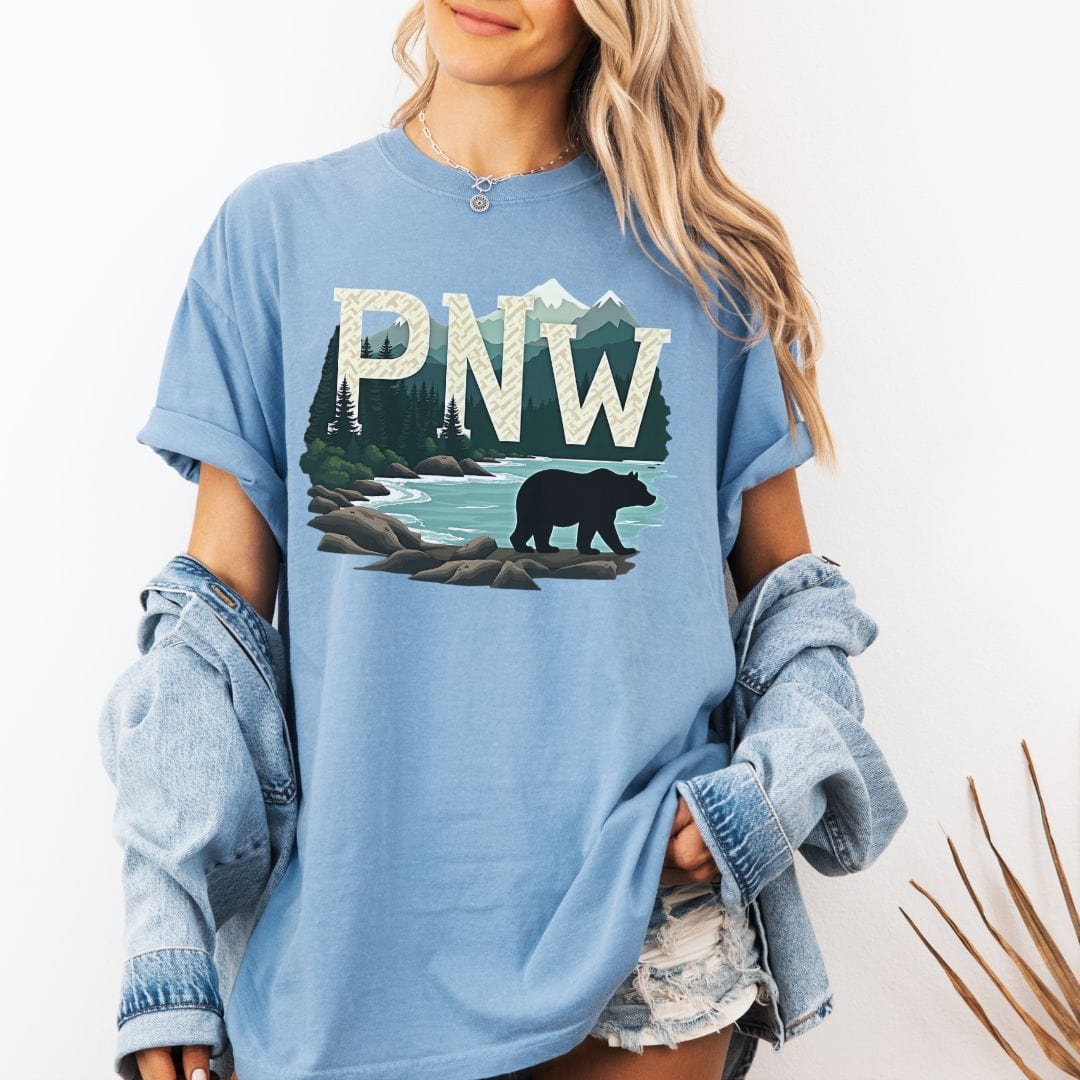 Woman wearing a washed denim t-shirt with PNW graphic featuring a bear and mountains on a white background