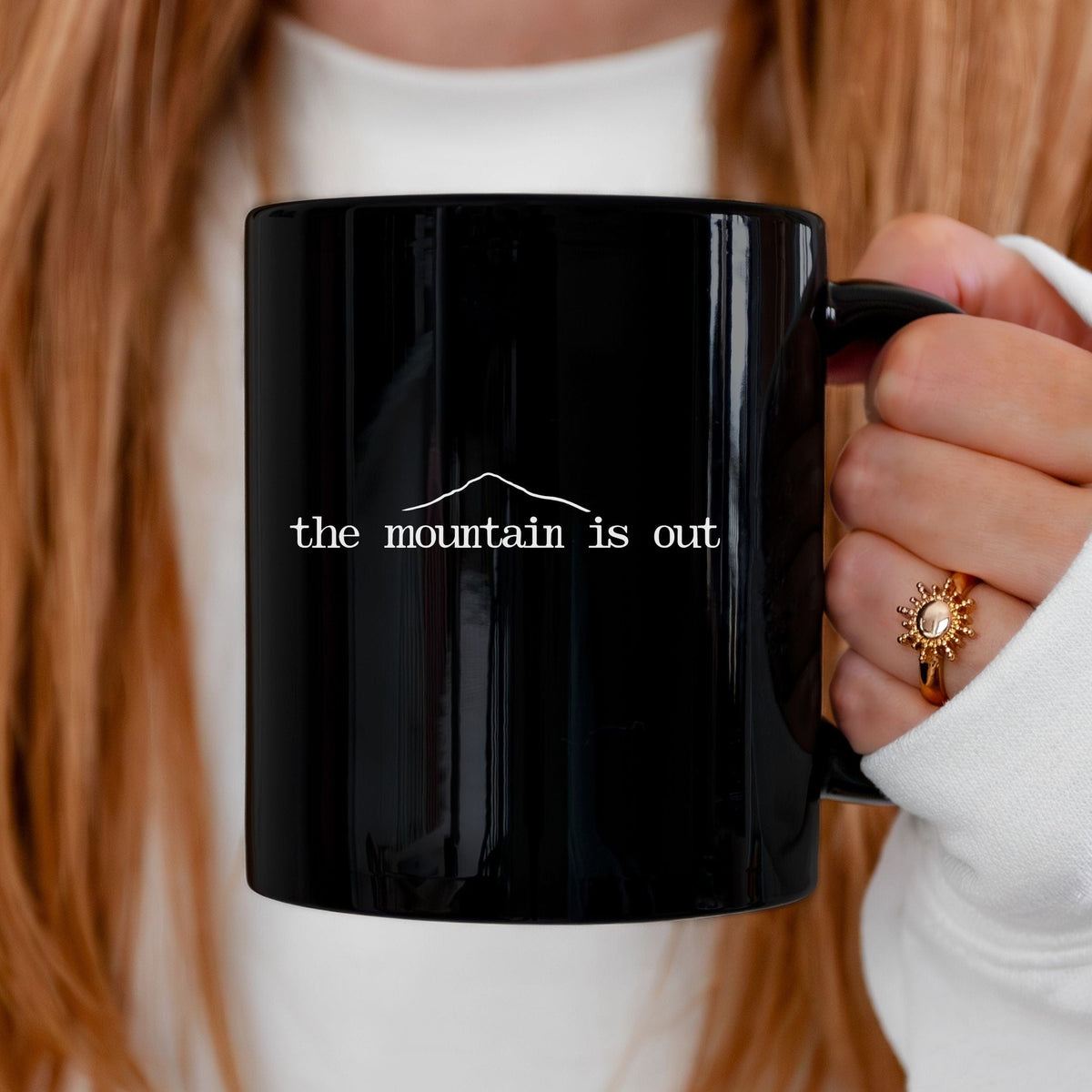 Person holding a black mug with 'the mountain is out' text