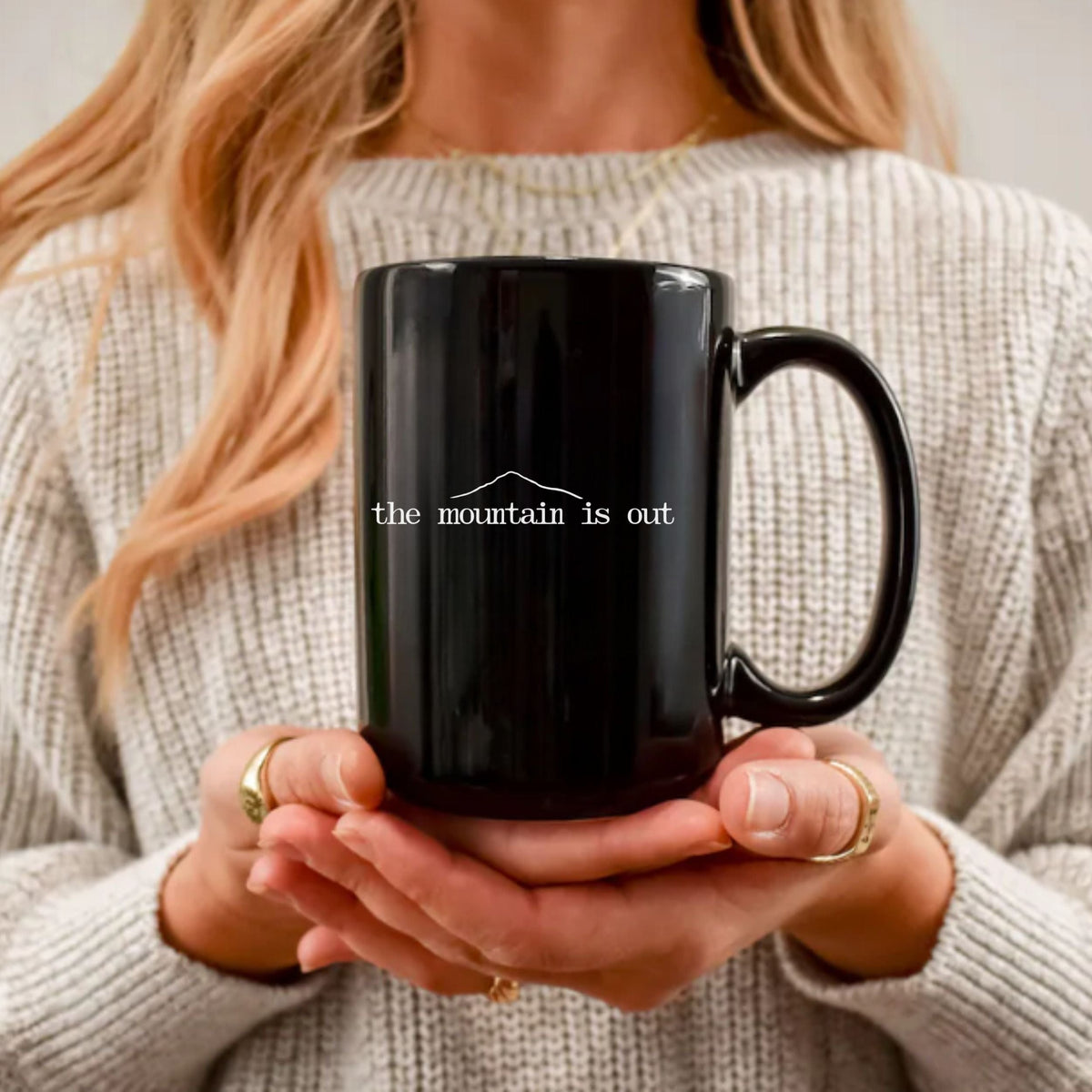 Person holding a black mug with 'the mountain is out' text