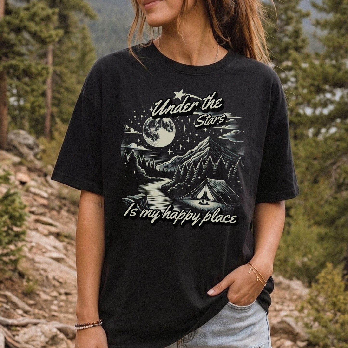 Woman wearing a black Under the Stars camping T-shirt with a moonlit mountain, forest, and night sky graphic.