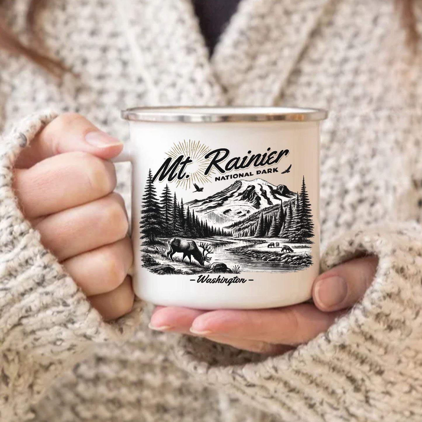 Person holding a white enamel camp mug with a vintage black-and-white Mt. Rainier National Park, Washington design.