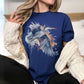 A woman wearing a navy blue crewneck t-shirt with a detailed watercolor graphic of a flying heron, styled with a cream cable-knit sweater draped off her shoulders.